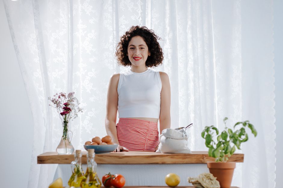 Cheerful woman with curly hair preparing fresh ingredients in a sunlit kitchen setting.