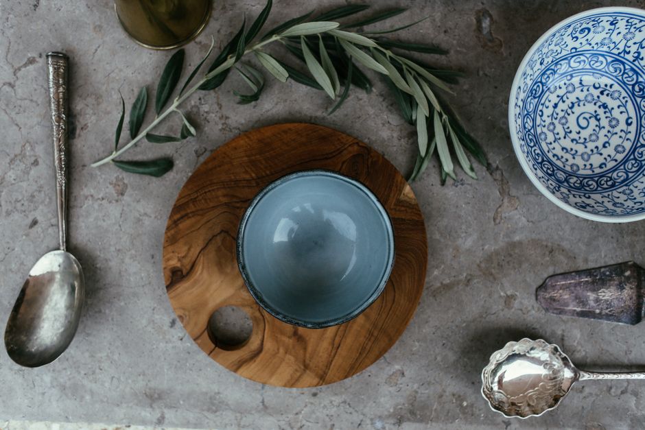 Top view of a rustic table setting with ceramic bowls, silver spoons, and an olive branch decor.