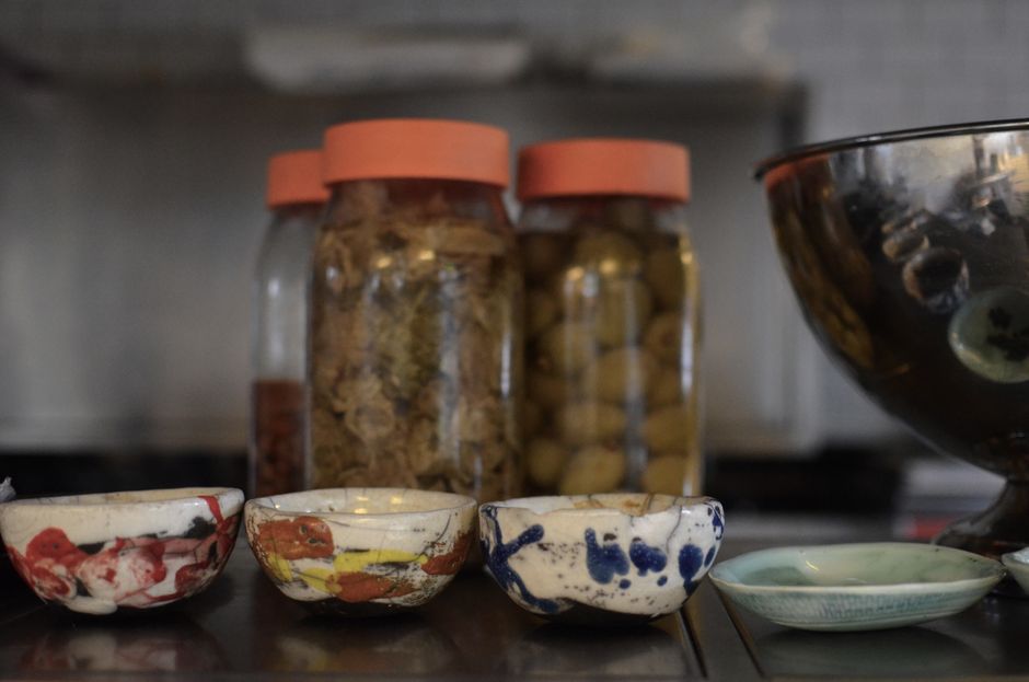 Artistic close-up of colorful ceramic bowls and jars of fermented food on a kitchen counter.