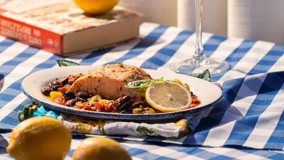 Grilled salmon served with olives, tomatoes, and lemon on a checkered tablecloth.
